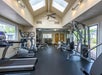 A fitness room with treadmills, exercise bikes, weight machines, and free weights. Skylights and windows provide natural lighting.