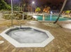A hot tub and a round swimming pool, surrounded by palm trees, are illuminated at night.