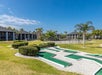 Outdoor view of a recreational area featuring a mini-golf course and a tennis court, surrounded by grass and palm trees under a clear blue sky.