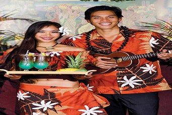 Two people in matching orange Hawaiian outfits, one holding tropical drinks on a tray, the other playing a ukulele, standing in front of a colorful background.