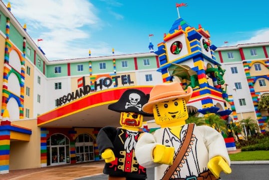Two LEGO character mascots, a pirate and an explorer, stand in front of the colorful entrance to the LEGOLAND Hotel.