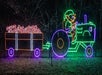 A neon holiday light display shows an elf driving a tractor pulling a trailer filled with candy canes.