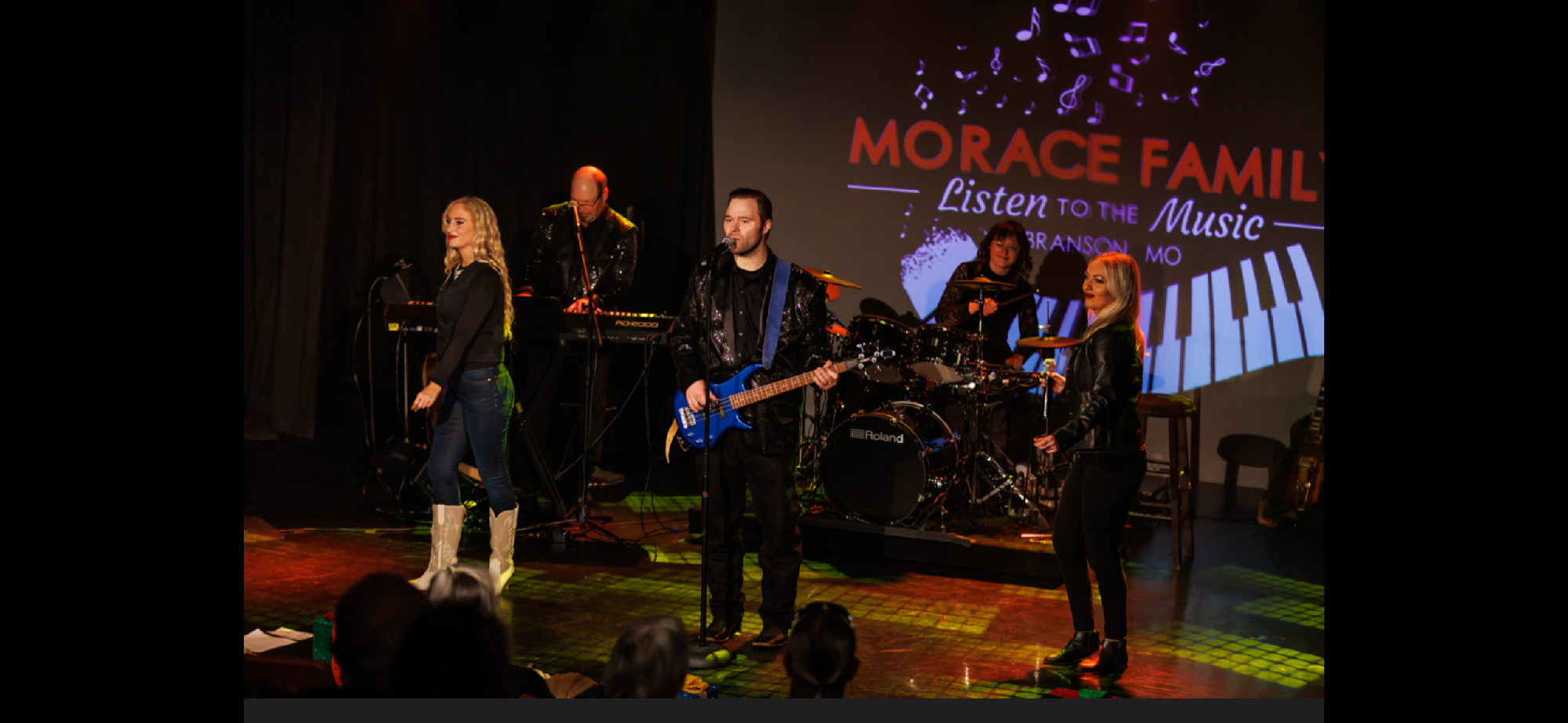 A band performs on stage with instruments and microphones; a large screen behind them displays "Morace Family Listen to the Music" with a piano graphic.