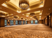 Spacious, elegantly lit ballroom with patterned carpet, large windows, and multiple chandeliers.