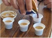 A person pours coffee into small plastic cups on a wooden table, with a lid nearby.