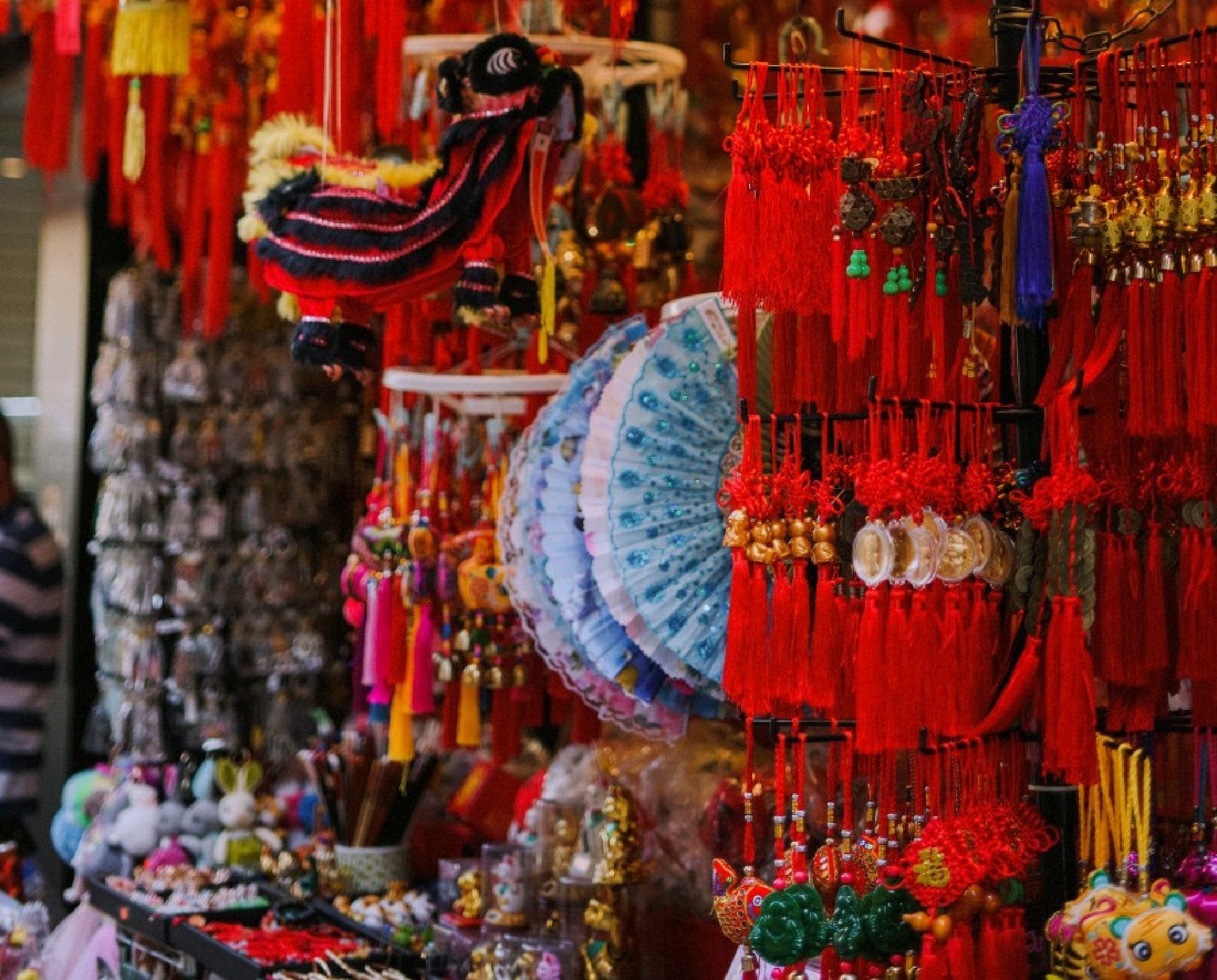 A market stall displays various traditional Asian decorations, including red tassels, fans, and hanging ornaments.