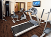 A small gym with a stationary bike, treadmill, a weight machine, and an elliptical with a TV mounted on the wall.