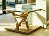 A bronze sculptural side table with a glass top and base, depicting abstract bird-like figures, stands near a large window, casting a shadow.