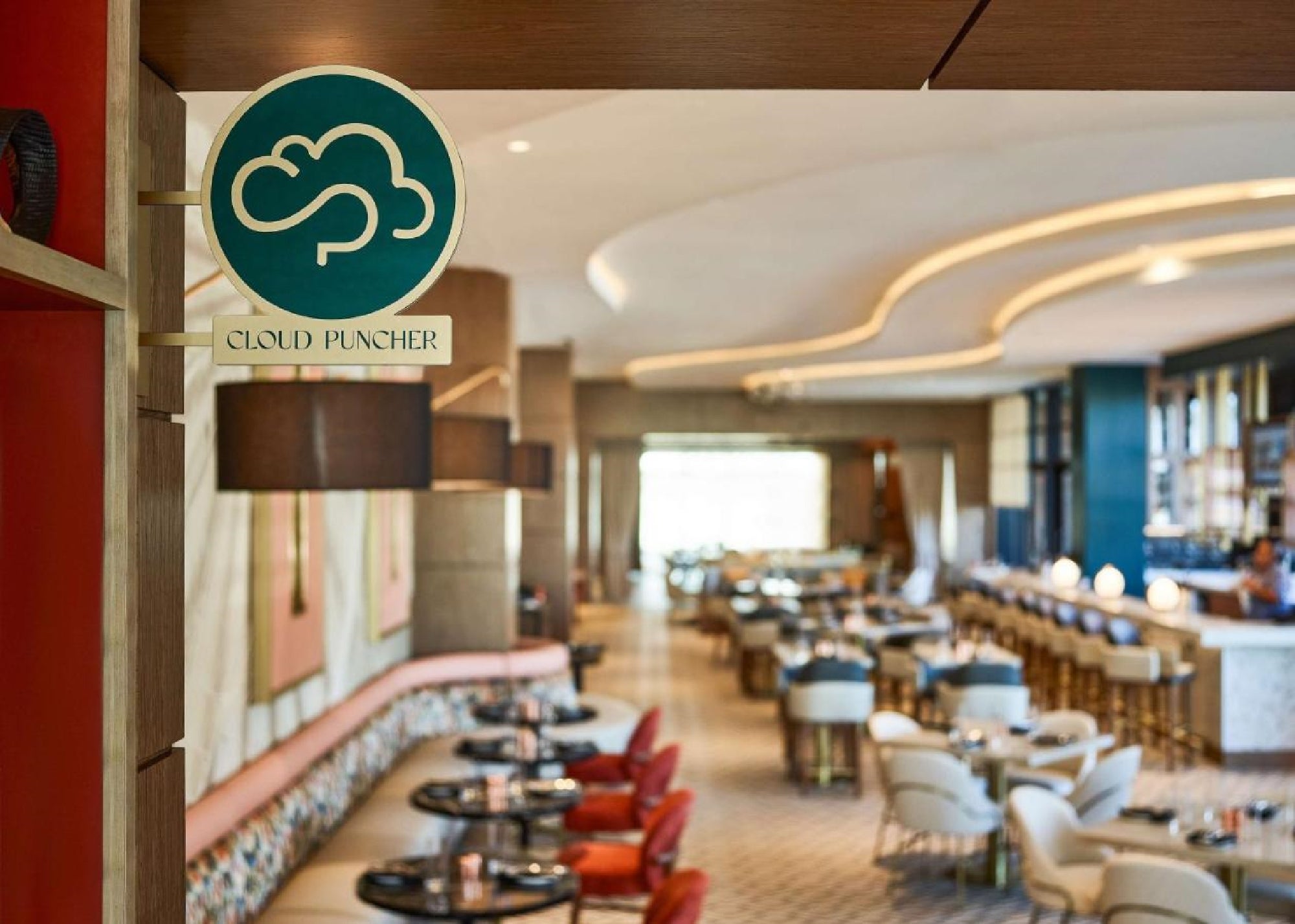 Modern restaurant interior with colorful seating, round tables, and a bar area. A sign reading "Cloud Puncher" is hanging on the left side.