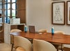 A conference room with a wooden table, beige chairs, a laptop, water bottles, framed abstract artwork, and a printer on a side table.