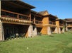 Wooden lodge building with multiple balconies, stone accents, and a well-kept lawn under a clear blue sky.