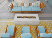 Modern outdoor seating area with wooden chairs and a sofa with blue cushions, arranged around a rectangular stone fire pit on a patterned yellow rug.