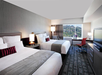 Experience a restful stay in a room with two queen beds and a large window showcasing the vibrant cityscape.