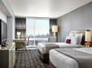 Experience a restful stay in a room with two queen beds and a large window showcasing the vibrant cityscape.