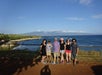 A family posting for a photo near an metal fence with the ocean in the background on a sunny day in Lahaina.