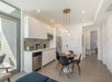 Modern kitchen and dining area with white cabinetry, stainless steel appliances, round table with four black chairs, and pendant lights. Hallway leads to a patterned accent wall.