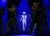 Performers in colorful striped suits and hats dance around a figure in a white suit and fedora on a dimly lit stage.