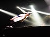 A performer in a white suit and hat leans forward dramatically on stage under bright spotlights.