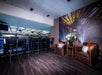 Luxury suite with bar stools, two brown armchairs, and floral arrangements. Large wall mural of an illuminated stadium adds ambiance.