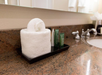 Rolled white towel and toiletries in a tray on a granite bathroom counter beside a silver faucet.