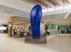 A large blue flip-flop sculpture is displayed in the center of a spacious, modern hotel lobby with seating areas and tropical decor.