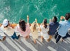 A line of people holding drinks looking over the railing of the boat into the blue green water on a sunny day on the Marina del Rey Brunch Cruise .