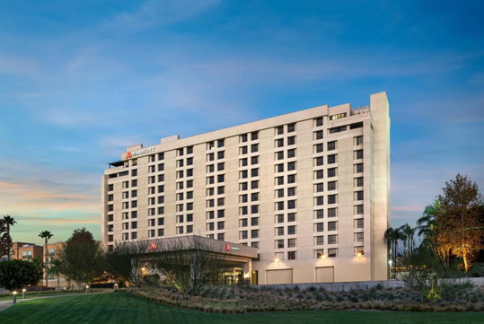 Tall hotel building with multiple windows, surrounded by trees and grassy area, under a clear sky at dusk.