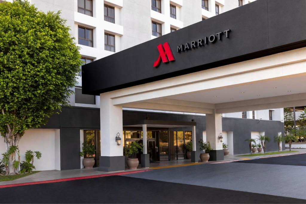Entrance of a Marriott hotel featuring a large logo, multiple windows, and potted plants by the doorway.