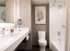 Modern bathroom with a white sink, large mirror, toilet, and bathtub. Walls are beige with an artwork of architectural columns above the toilet.