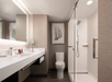 Modern bathroom with a glass-enclosed shower, a white toilet, and a wide vanity with a large mirror. A framed artwork hangs on the wall.