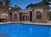 Brick house with a swimming pool in the foreground, featuring large windows and patio seating with an umbrella.