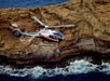 A Maverick airbus flying over the rocky Molokini, a partially submerged volcanic crater, with water crashing against it.