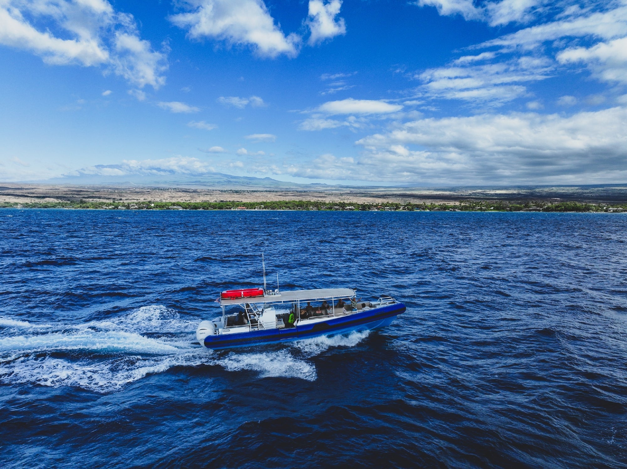 A blue and white motorboat travels across deep blue ocean water near a distant coastline under a partly cloudy sky.