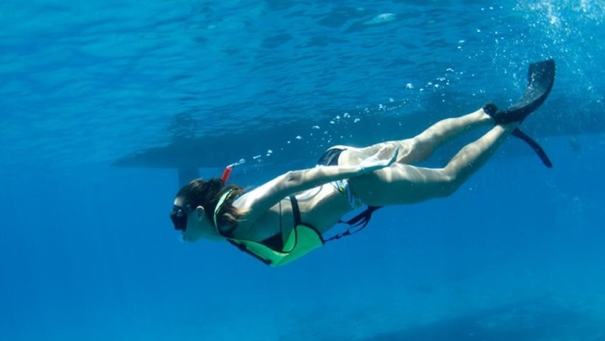 A person wearing snorkeling gear and fins swims underwater in clear blue water.