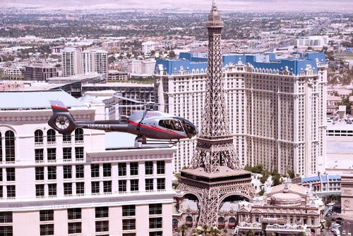 A helicopter flies past the replica Eiffel Tower and surrounding hotels on the Las Vegas Strip during the day.