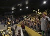 A costumed knight in black and yellow greets an enthusiastic audience waving yellow flags in an indoor arena.