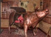 A lifelike model of a bronze bull with an open door in its side, revealing a bloody, human-like figure inside; firewood is arranged beneath the bull.