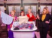 Four women stand behind a table holding various bras and panties, displaying them with expressive gestures.