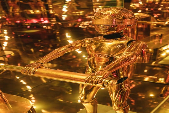 A golden robot with a futuristic design stands in a reflective gold environment, holding a horizontal bar.