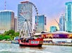 A red and black pirate ship sails past a Ferris wheel near a Hard Rock Cafe, with modern city buildings in the background.