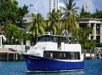 A blue and white colored boat with a name painted "Manatee ll" with passengers on board cruising along the famous Miami's Biscayne Bay showing its breathtaking views of well-known homes and buildings along the bay.
