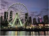 Ferris wheel illuminated at night against a city skyline with skyscrapers, reflecting on water.