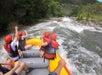 A group of people wearing helmets and life jackets are whitewater rafting down a river surrounded by trees and rocks.