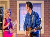 A Carl Perkins impersonator playing guitar on stage with a woman in a pink dress playing tambourine at the Million Dollar Quartet.