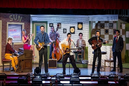 The cast of the Million Dollar Quartet on a 50s themed stage singing and playing various instruments.