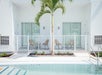 Backyard with a swimming pool, two patio chairs, a palm tree, and sliding glass doors on a white building.