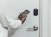 A person uses a smartphone app to unlock a digital door lock with a keypad.