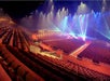 Large, empty theater with rows of red seats, a wide stage, and colorful stage lights illuminating the area.