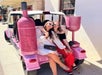 Two women sitting on the back of a pink vehicle with oversized pink wine bottle and glass decorations.