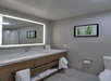 A single vanity lighted mirror, fresh towels, and toilet in a guest bathroom.